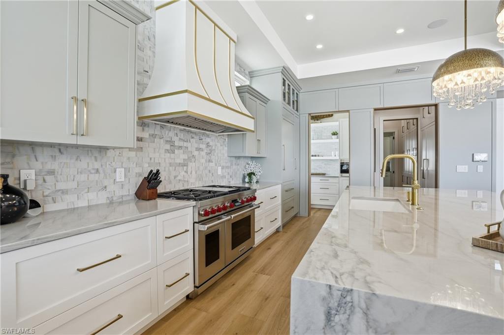 Kitchen with light stone countertops, range with two ovens, light wood-style flooring, decorative backsplash, and white cabinetry - Virtually Edited Image