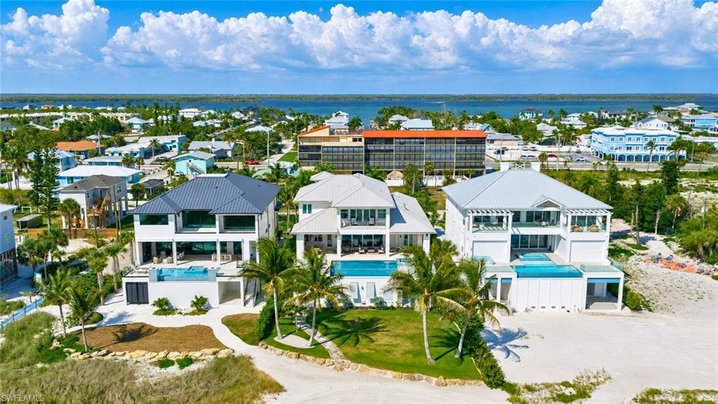 Modern architectural residence featuring a prominent metal roof, multiple balconies, a ground-level patio, an integrated swimming pool, and a surrounding landscaped yard with palm trees