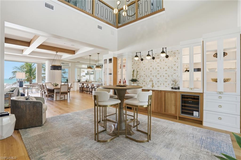 Dining room featuring light wood-style floors, wine cooler, a chandelier, a high ceiling, and wet bar - Virtually Edited Image