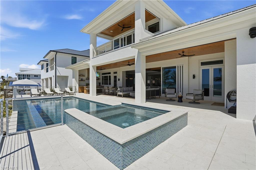 Rear view of house featuring a balcony, a ceiling fan, an outdoor hangout area, a patio area, and a pool with connected hot tub - Virtually Edited Image