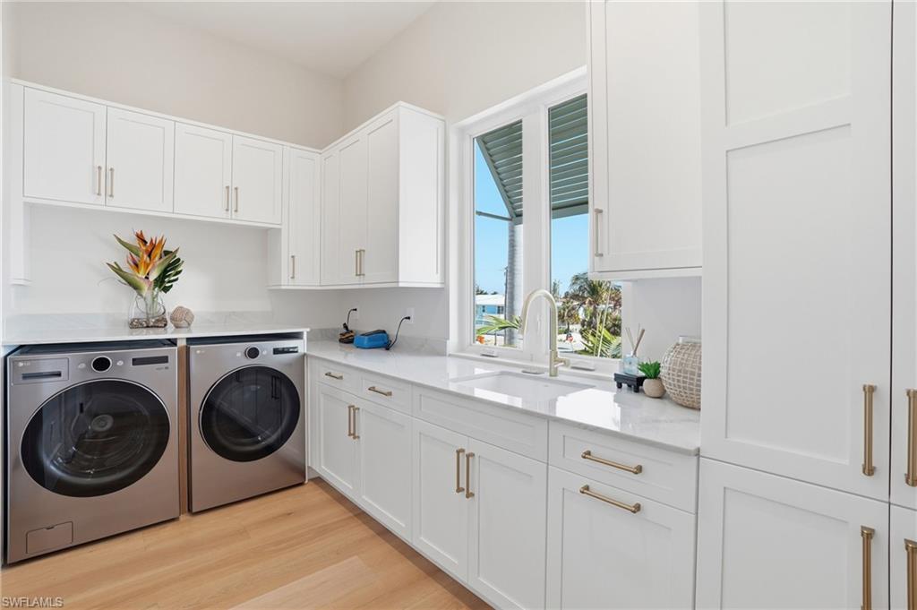 Laundry area featuring cabinet space, light wood-type flooring, and separate washer and dryer - Virtually Edited Image