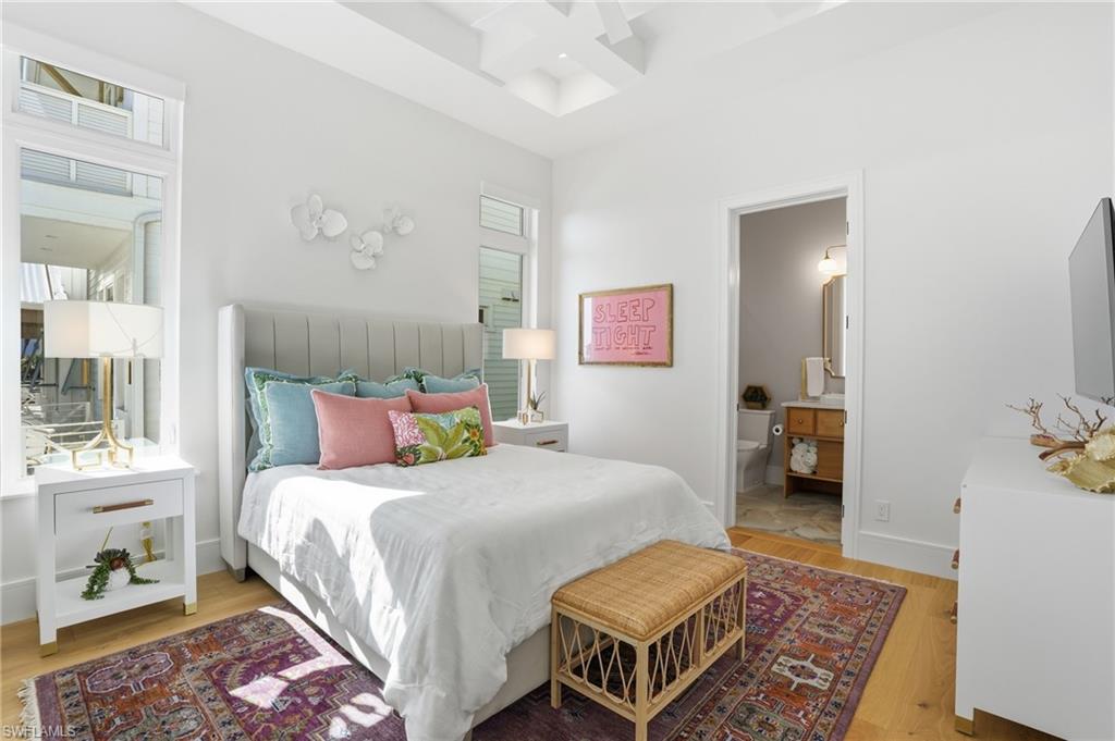 Bedroom featuring coffered ceiling, light wood-type flooring, and ensuite bathroom - Virtually Edited Image