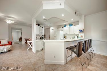 Kitchen with light countertops, a peninsula, white cabinets, a kitchen bar, and recessed lighting