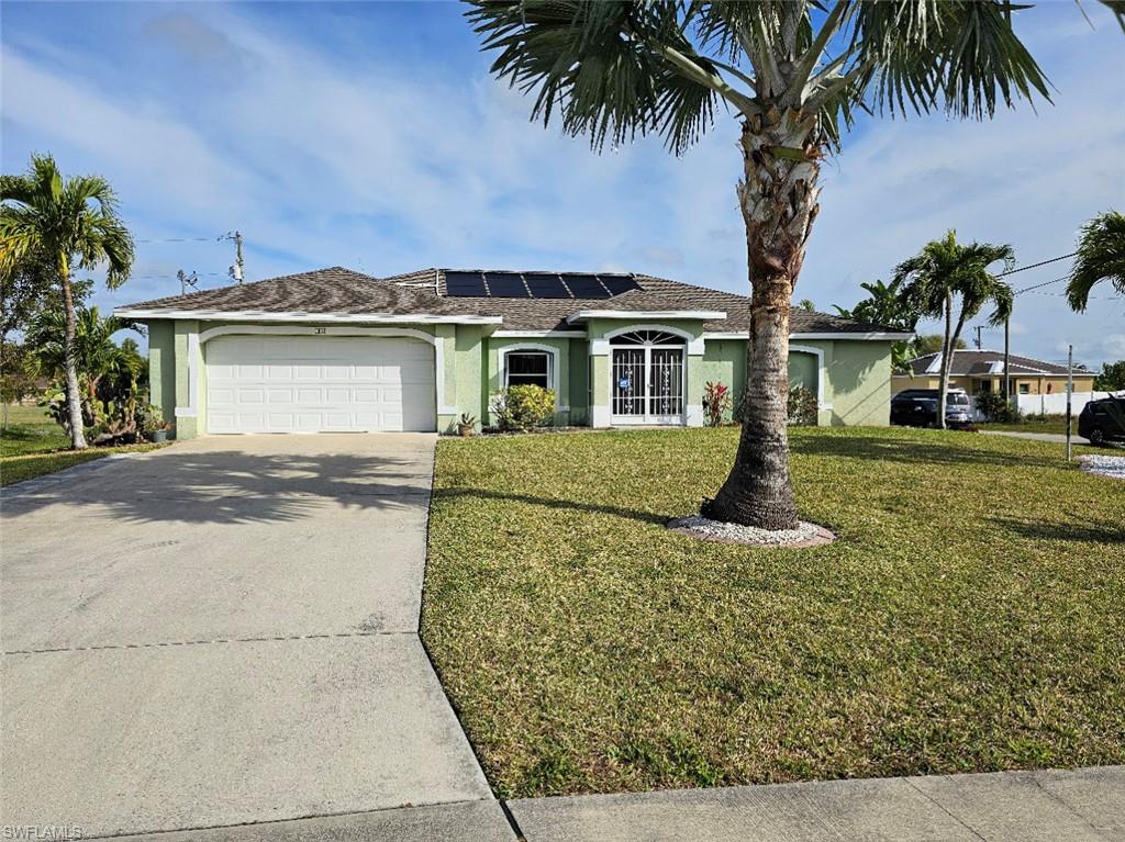 Single story home featuring stucco siding, roof mounted solar panels, an attached garage, and driveway