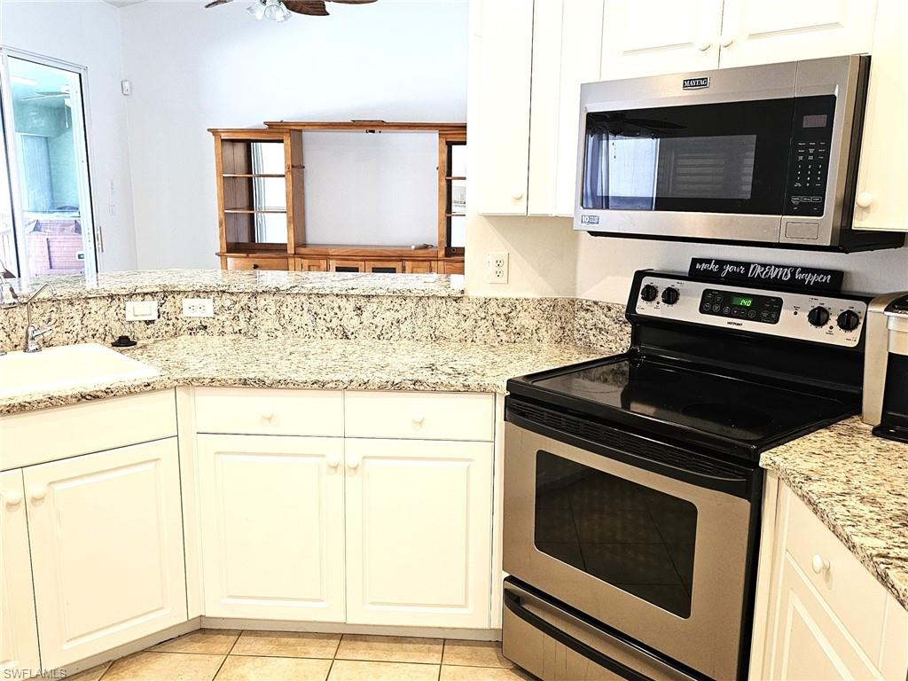 Kitchen with stainless steel appliances, light stone countertops, white cabinets, and a ceiling fan