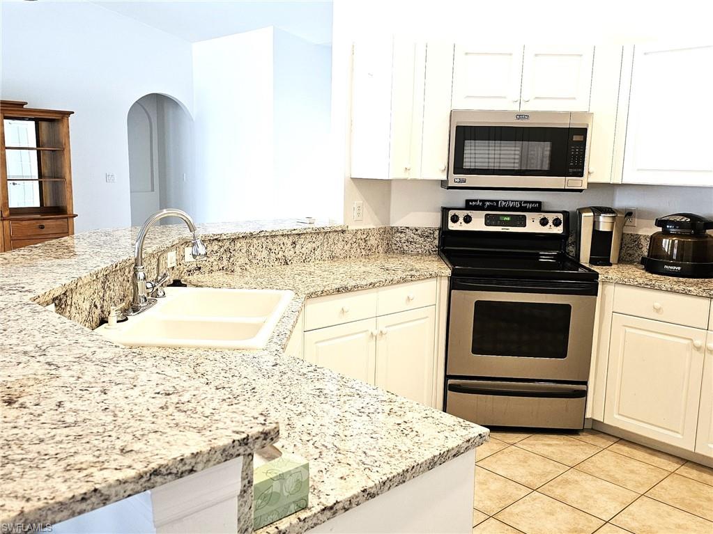 Kitchen with stainless steel appliances, white cabinetry, light stone counters, and light tile patterned floors