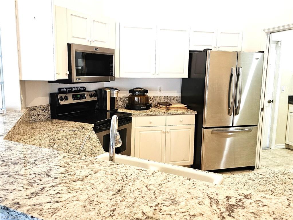 Kitchen featuring stainless steel appliances, white cabinets, light stone counters, and light tile patterned flooring