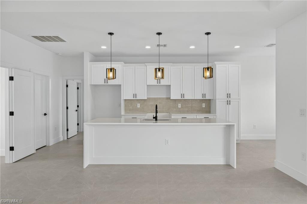 Kitchen with white cabinetry, a spacious island, and decorative light fixtures