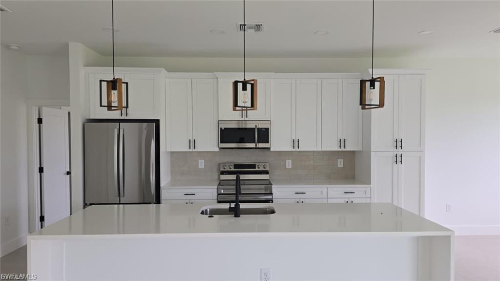 Kitchen featuring stainless steel appliances, hanging light fixtures, light stone countertops, a kitchen island with sink, and white cabinetry