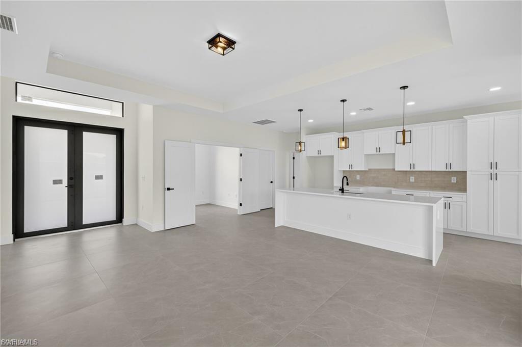 Kitchen with a center island with sink, white cabinets, hanging light fixtures, open floor plan, and tasteful backsplash