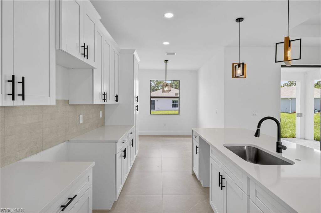 Kitchen featuring white cabinets, decorative light fixtures, light stone counters, and backsplash