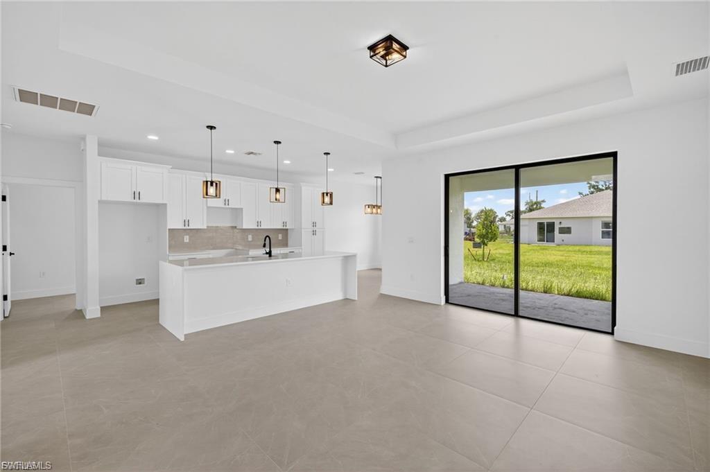 Kitchen with white cabinets, pendant lighting, a tray ceiling, a large island, and open floor plan