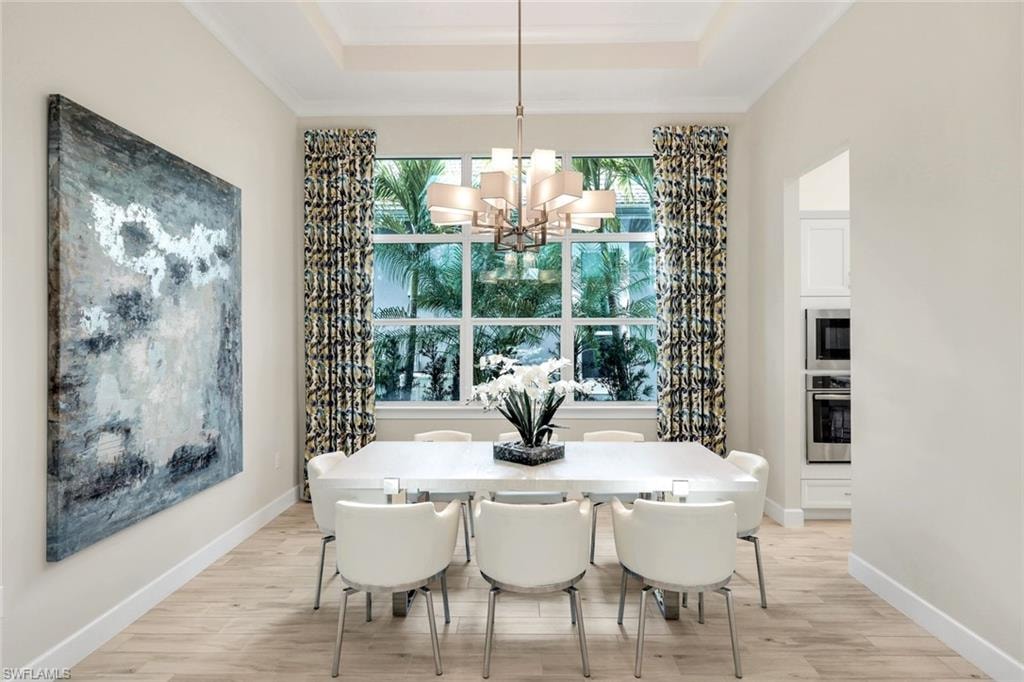 Dining area with hanging lights, light wood-style floors, and a tray ceiling