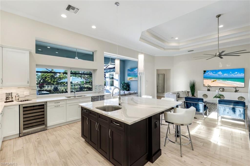 Kitchen with light stone counters, wine cooler, two tone color scheme, open floor plan, and an island with sink
