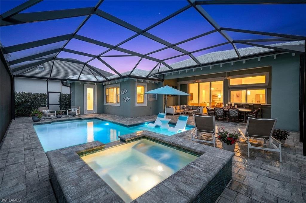 Pool at dusk with outdoor furniture, a sunroom, a pool with connected hot tub, and glass enclosure
