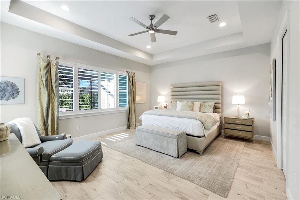Bedroom featuring a raised ceiling, light wood finished floors, recessed lighting, and ceiling fan