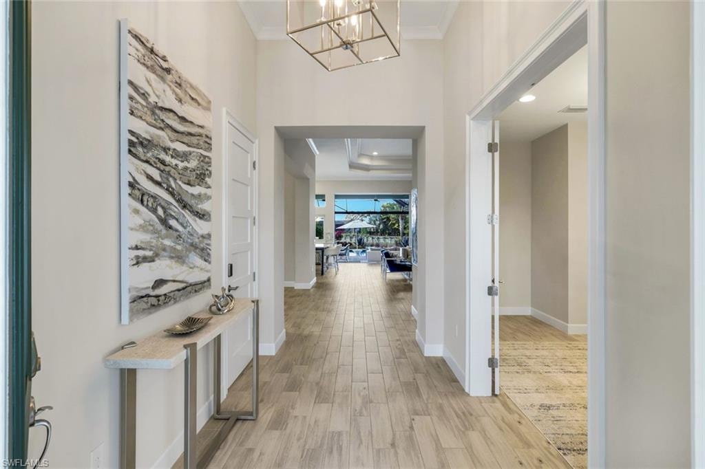 Hall featuring light wood-type flooring, hanging lights, ornamental molding, and a high ceiling