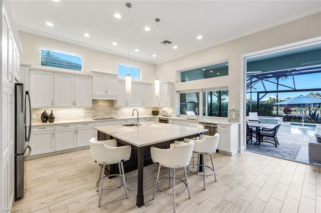 Kitchen featuring a breakfast bar, white cabinets, a sunroom, decorative light fixtures, and crown molding