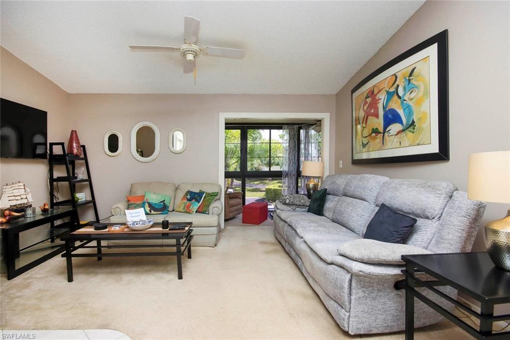 Living room with ceiling fan, lofted ceiling, and light colored carpet