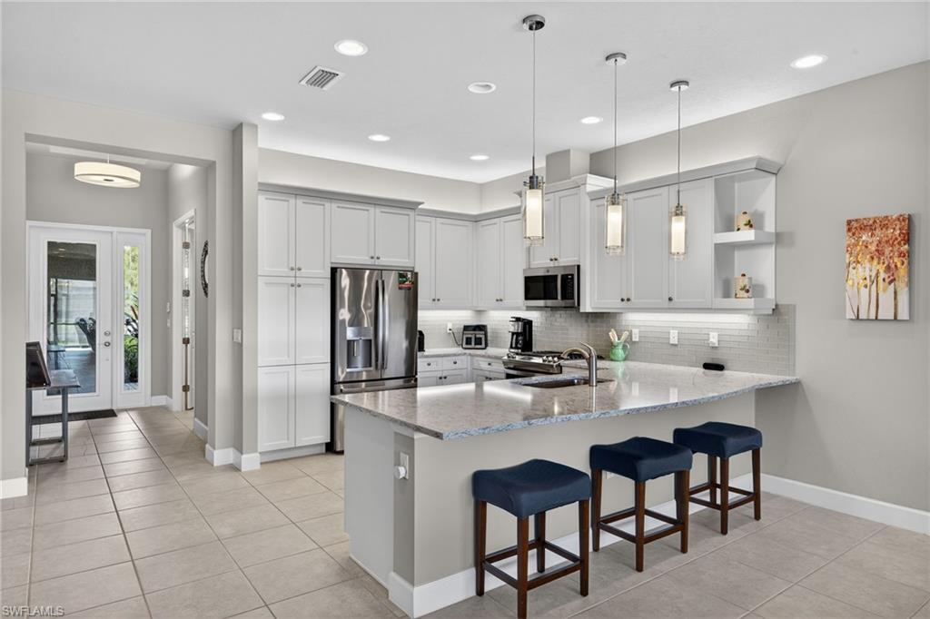 Kitchen with a peninsula, a breakfast bar area, stainless steel appliances, open shelves, and light stone countertops