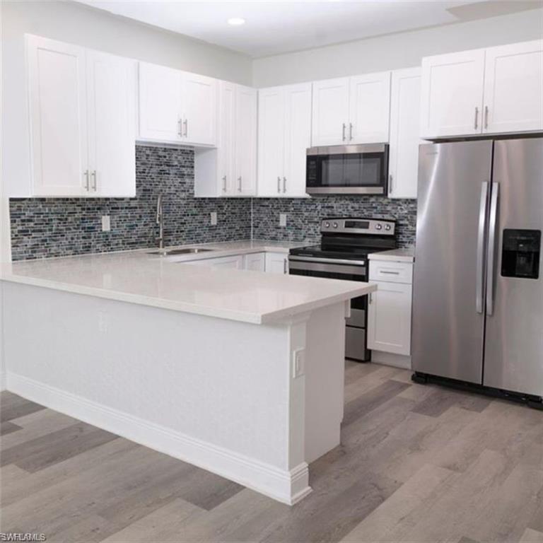 Kitchen with stainless steel appliances, white cabinetry, a peninsula, light wood-style flooring, and light stone countertops
