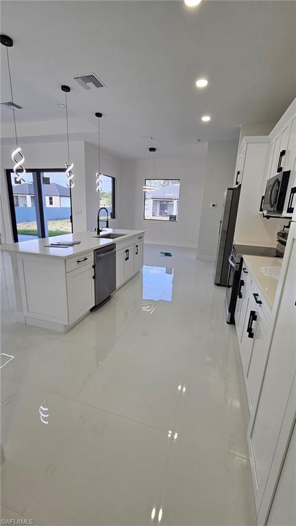 Kitchen featuring white cabinets, pendant lighting, stainless steel appliances, and light stone countertops