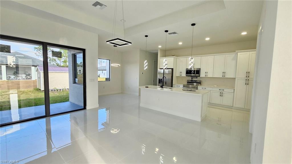 Kitchen featuring white cabinetry, hanging light fixtures, a center island with sink, stainless steel appliances, and light tile patterned floors