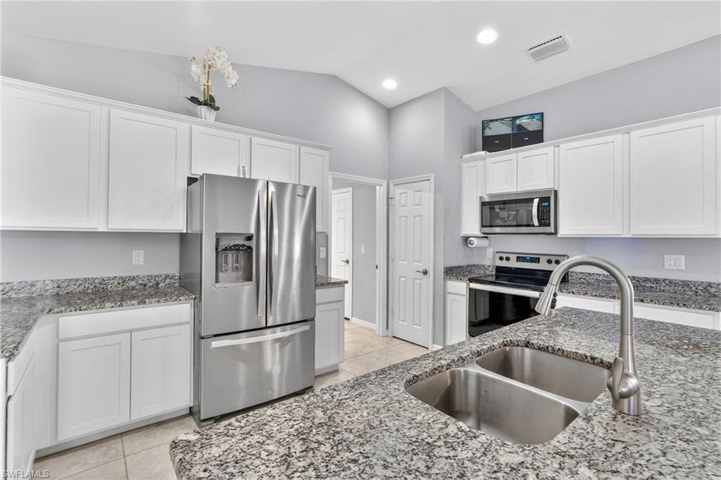 Kitchen featuring stainless steel appliances, white cabinets, lofted ceiling, light tile patterned floors, and light stone counters