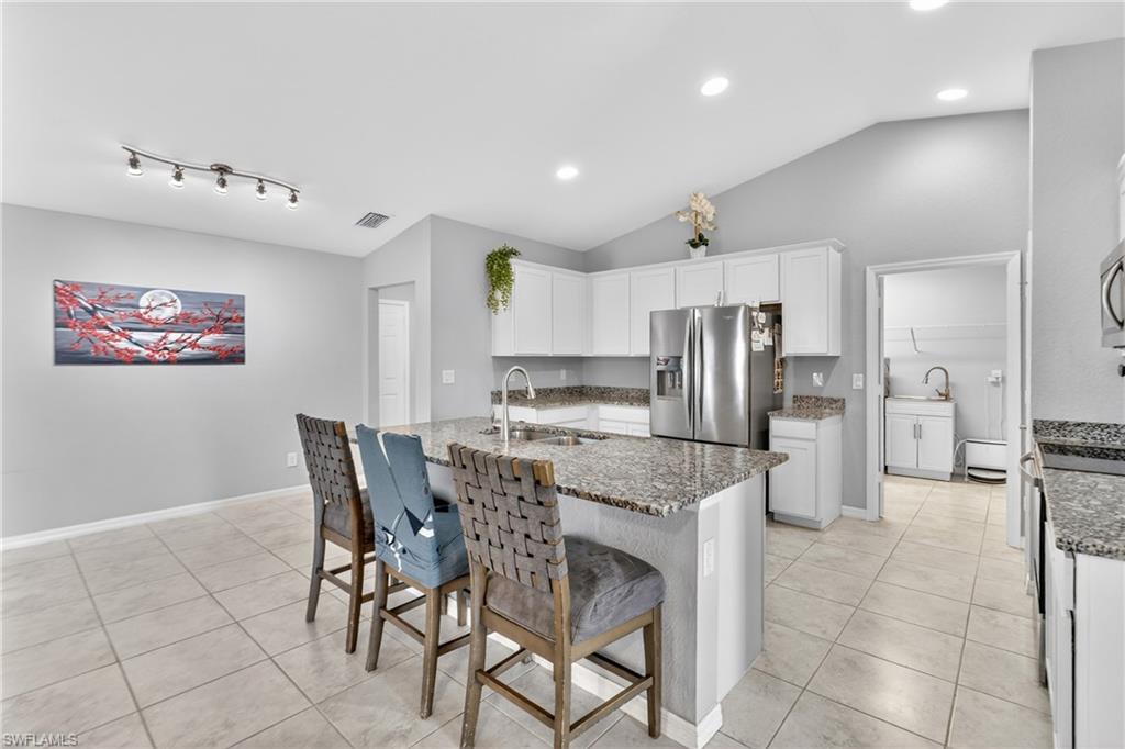 Kitchen with white cabinetry, light stone countertops, stainless steel appliances, light tile patterned floors, and lofted ceiling
