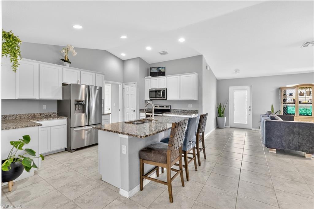 Kitchen with stainless steel appliances, a breakfast bar area, dark stone countertops, white cabinets, and lofted ceiling