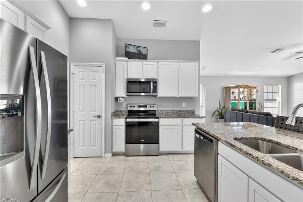 Kitchen with stainless steel appliances, white cabinetry, light stone countertops, open floor plan, and light tile patterned floors