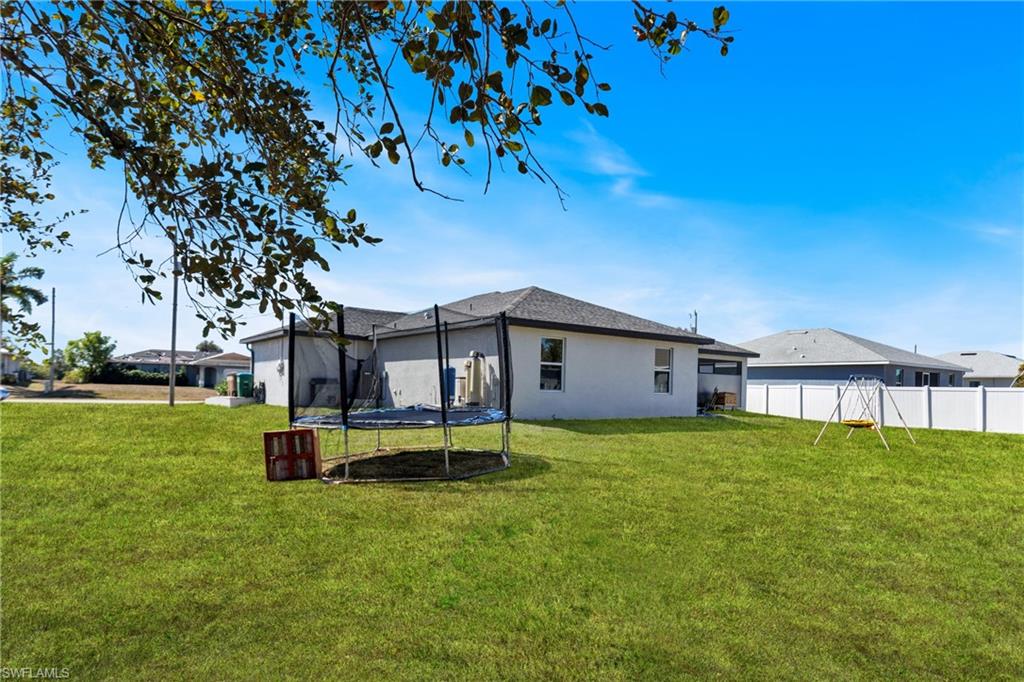 Back of property with a trampoline, stucco siding, and a lawn