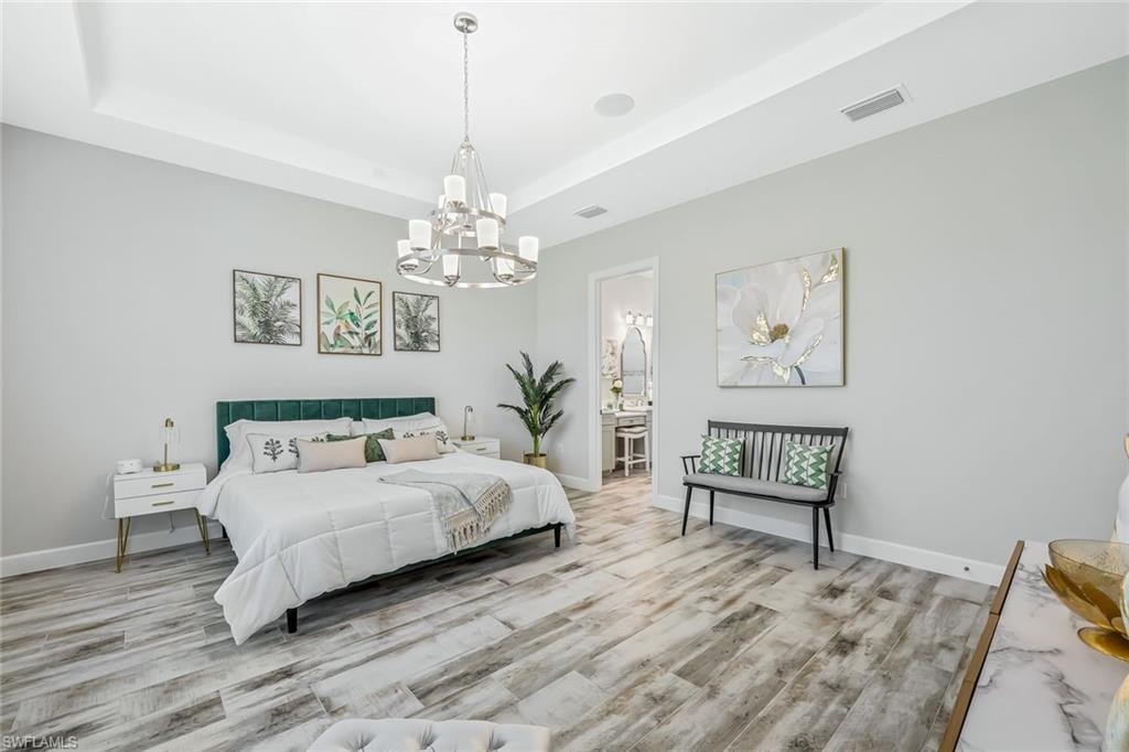 Bedroom featuring a chandelier, a raised ceiling, wood finished floors, and ensuite bath