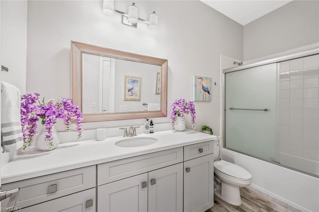 Full bath featuring vanity, shower / bath combination with glass door, and wood finished floors