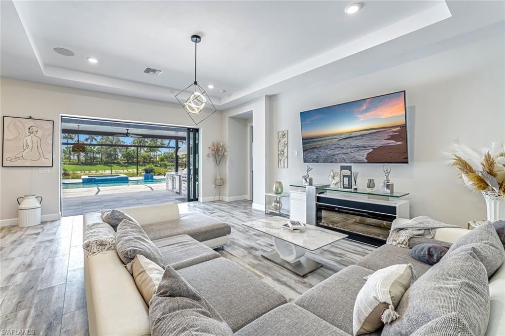 Living area featuring a raised ceiling, light wood-style floors, and recessed lighting