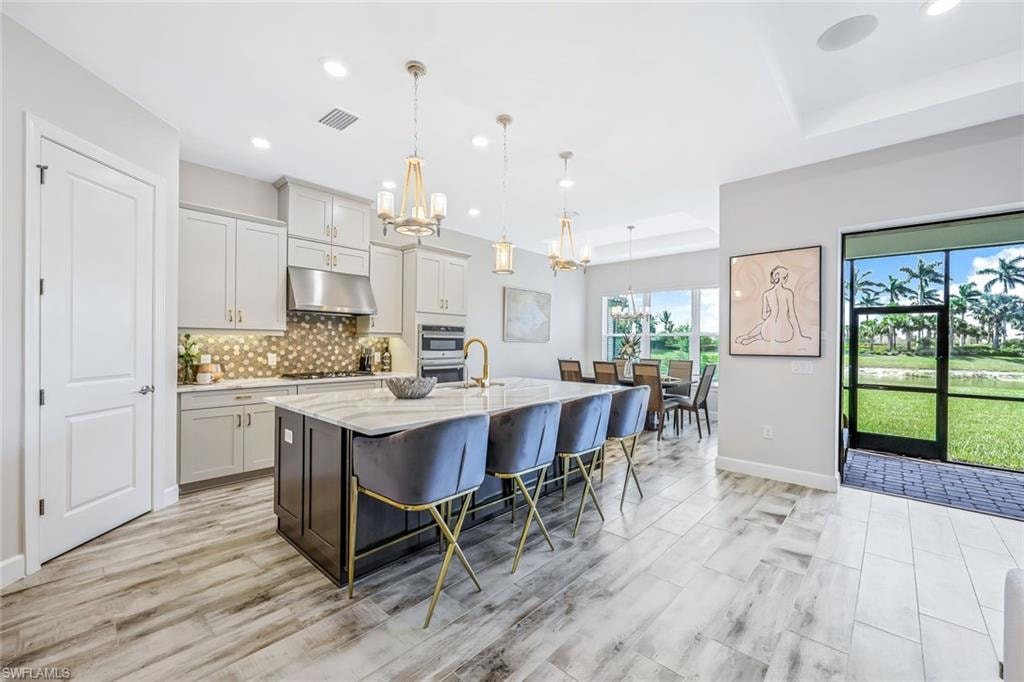 Kitchen featuring under cabinet range hood, a chandelier, a kitchen island with sink, light stone counters, and gas stovetop