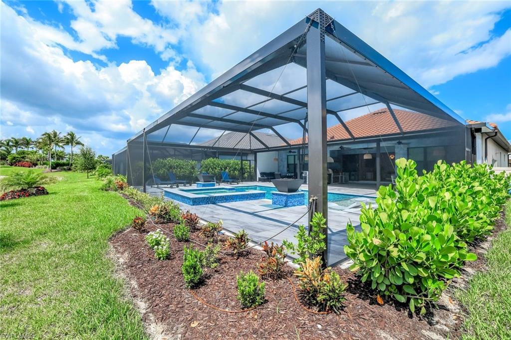 View of swimming pool featuring a lawn, a pool with connected hot tub, a patio area, and glass enclosure