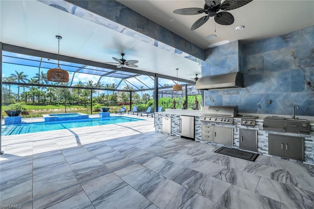 View of pool featuring an outdoor kitchen, a ceiling fan, a pool with connected hot tub, glass enclosure, and a patio