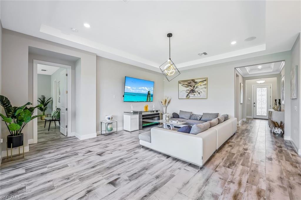 Living area with a raised ceiling, light wood-style flooring, recessed lighting, and plenty of natural light