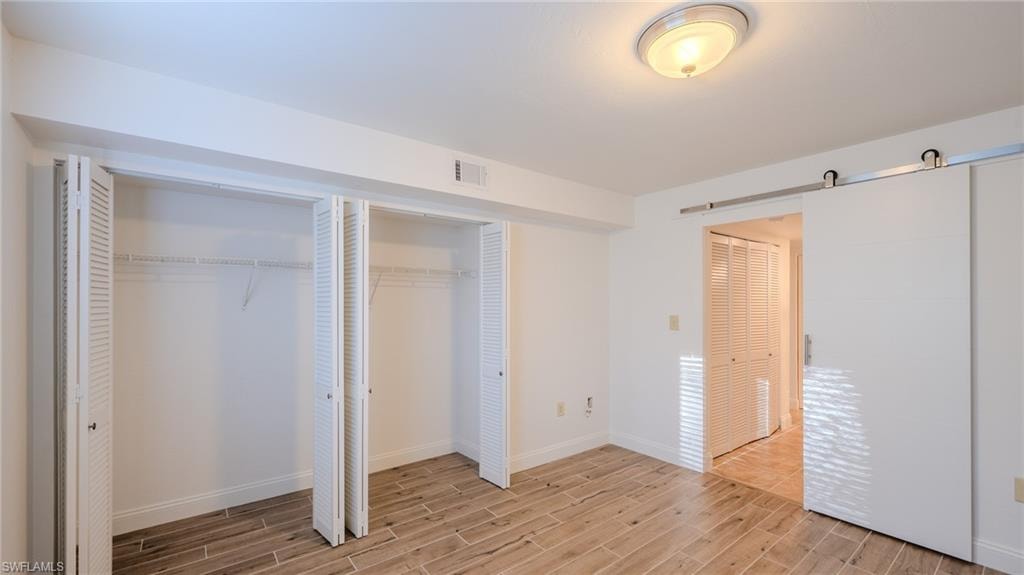 Unfurnished bedroom with a barn door, wood tiled floors, and multiple closets