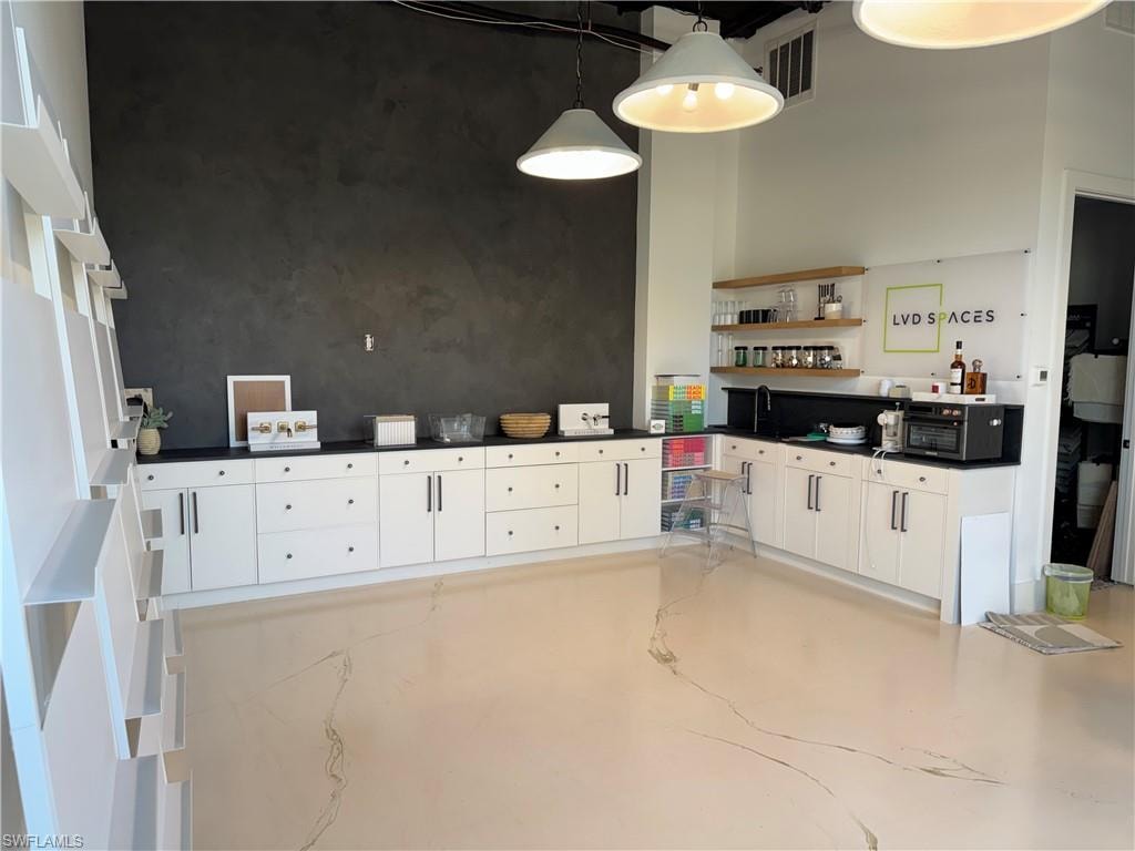 Kitchen with white cabinets, concrete floors, decorative light fixtures, dark countertops, and a high ceiling