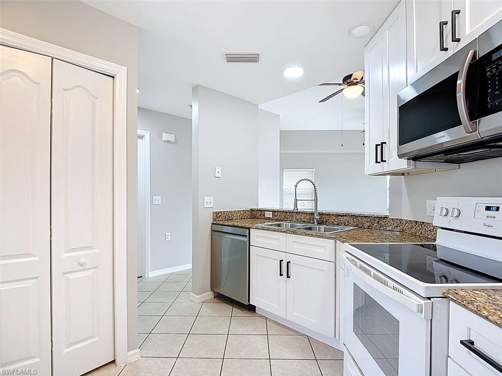 Kitchen featuring stainless steel appliances, dark stone counters, ceiling fan, white cabinetry, and light tile patterned floors