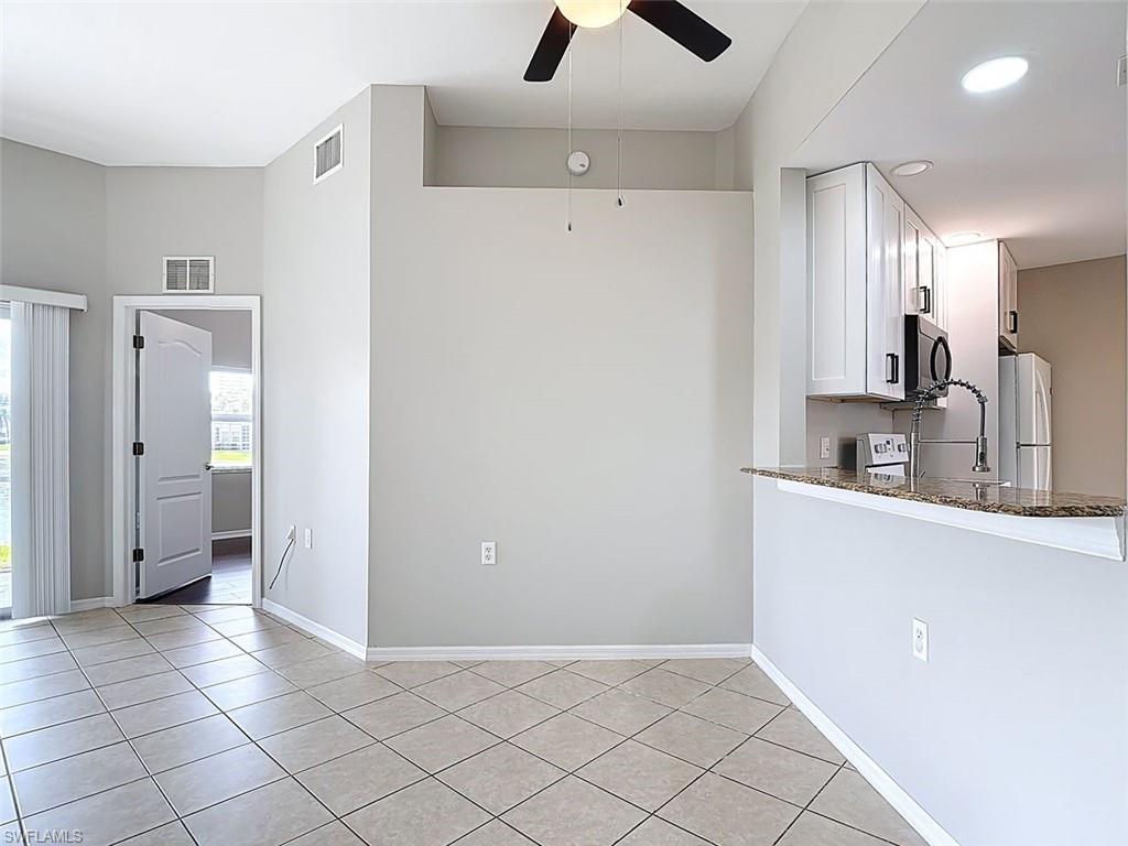 Kitchen featuring a ceiling fan, white cabinets, dark stone countertops, freestanding refrigerator, and light tile patterned floors