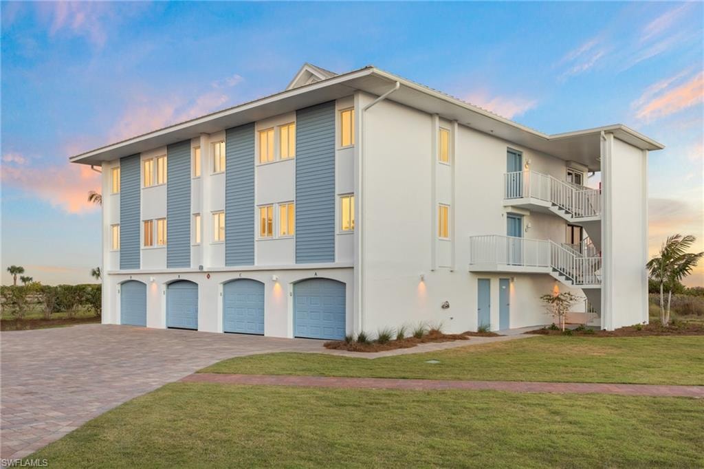 View of front of property with a lawn, a balcony, decorative driveway, stucco siding, and an attached garage