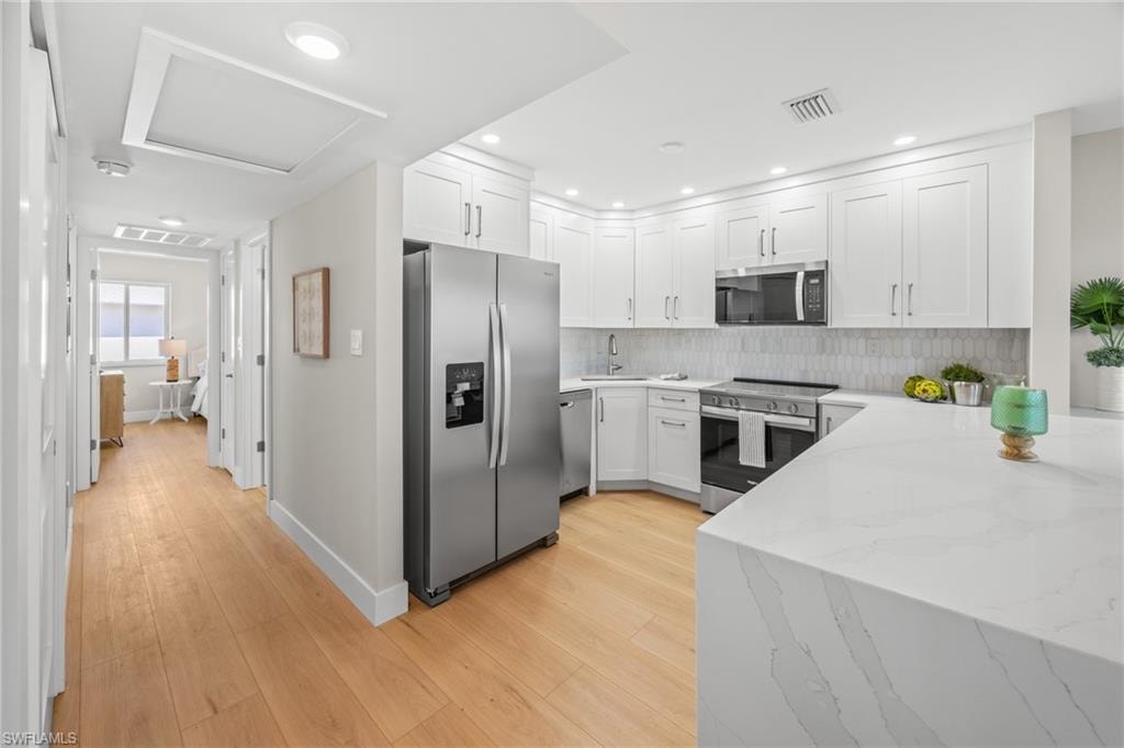 Kitchen with stainless steel appliances, white cabinets, light stone counters, light wood finished floors, and a peninsula