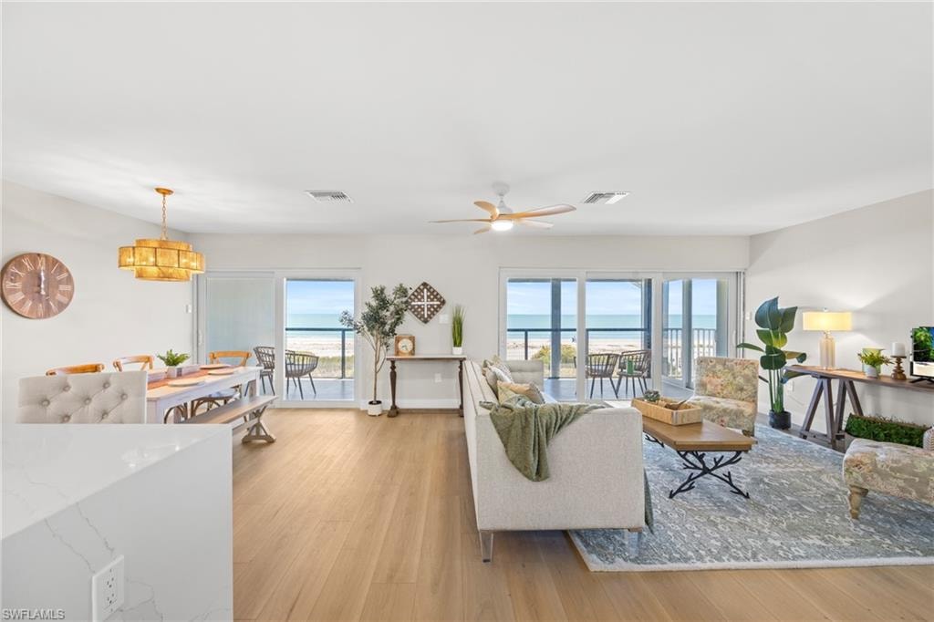 Living room with light wood-type flooring, ceiling fan, a water view, and hanging lights