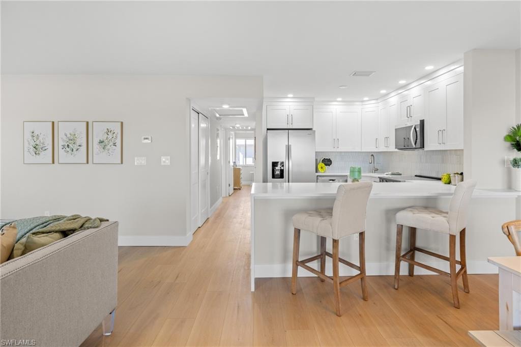 Kitchen featuring a kitchen breakfast bar, stainless steel appliances, a peninsula, light wood-style floors, and white cabinets