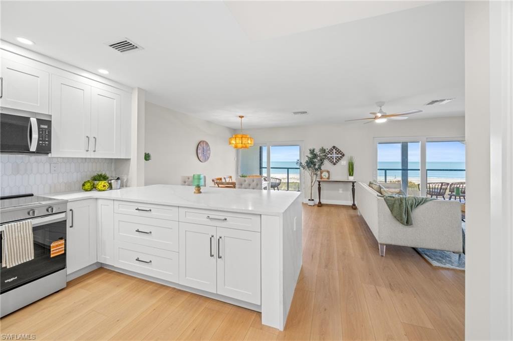 Kitchen featuring stainless steel appliances, decorative backsplash, white cabinetry, a peninsula, and light wood-style flooring