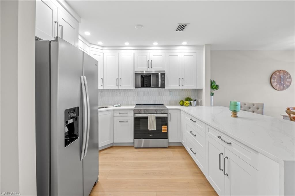 Kitchen featuring stainless steel appliances, light stone counters, a peninsula, white cabinets, and recessed lighting