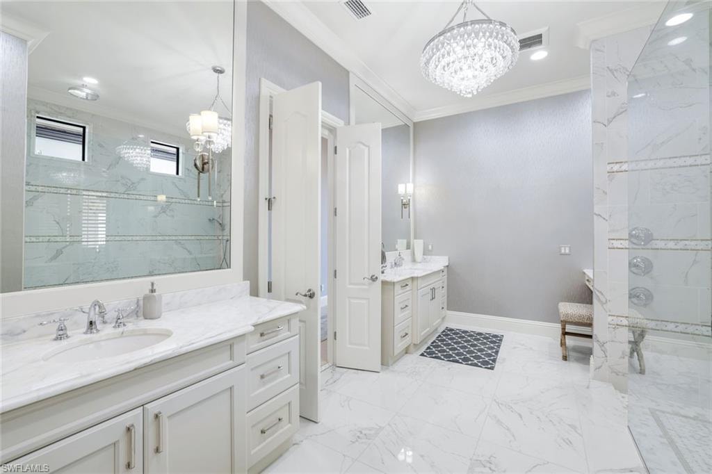 Bathroom featuring a chandelier, crown molding, two vanities, a marble finish shower, and light marble finish flooring
